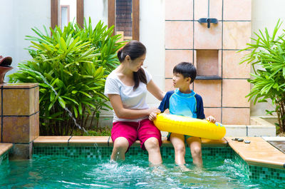 Mother looking at son sitting with inflatable ring at poolside