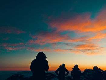 Silhouette people standing by hills against sky during sunset