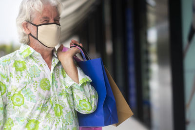 Close-up of smiling man holding shopping bag outdoors