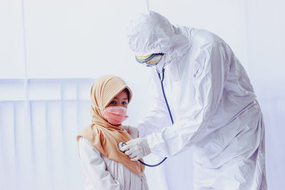 Portrait of young woman standing against white wall