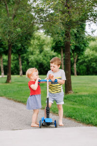 Siblings fighting for fight scooter on road at park