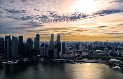 Aerial view of cityscape at waterfront against cloudy sky