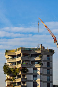 Low angle view of crane by building against sky