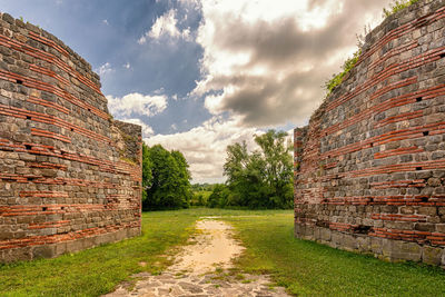 Stone wall of old building on field against sky