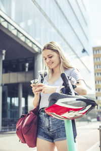 Portrait of smiling young woman leaning on handlebar of e-scooter using cell phone, berlin, germany