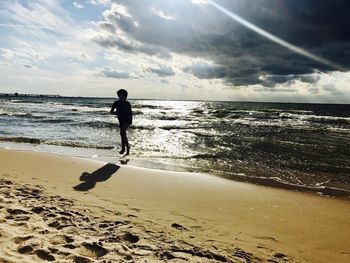 Silhouette boy in sea against sky during sunset
