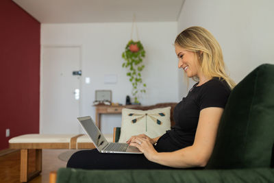 Woman working at home from couch with laptop on her lap. home office concept. gray notebook