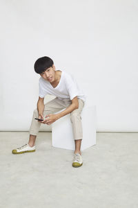Full length of young man sitting against white background