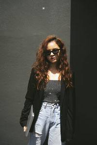 Portrait of young woman standing against wall