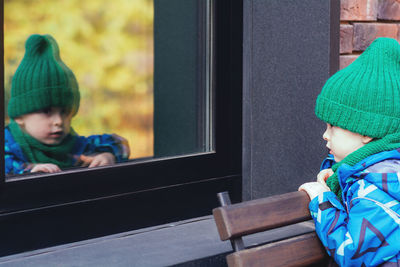 A small child looks out the window from the street. the boy sees his reflection in the mirror window