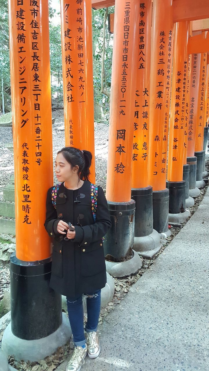orange color, real people, one person, full length, text, communication, lifestyles, script, non-western script, day, religion, leisure activity, casual clothing, belief, outdoors, architecture, standing, shrine