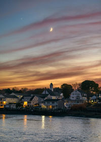 Scenic view of moon in colorful sky after sunset over a colonial beach town in maine against the sea