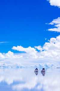 Distant view of tourists on cars by lake against blue sky