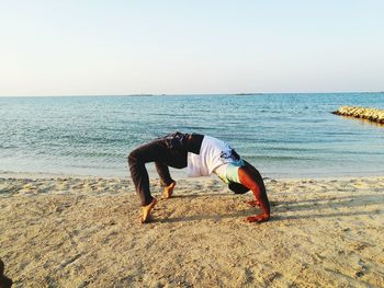 Man practicing backflipping on sand against sea at beach