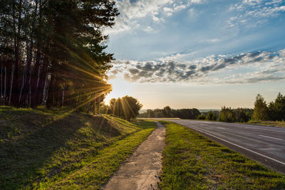 Empty road by trees against sky during sunrise