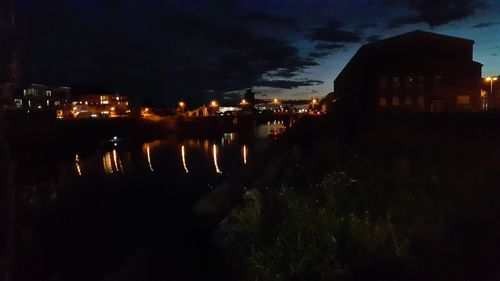Illuminated buildings by river against sky at night