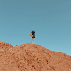 Rear view of man walking on mountain against clear blue sky