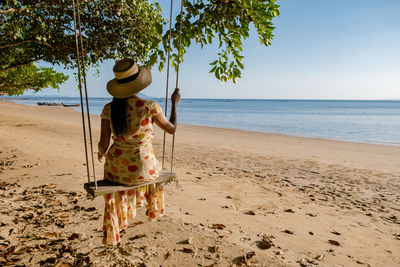 Rear view of woman sitting on rope swing at beach