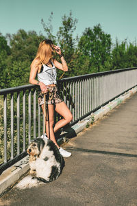 Woman standing by dog on footpath while leaning on railing