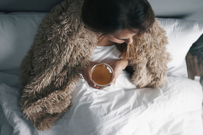 Directly above shot of woman holding lemon tea sitting on bed