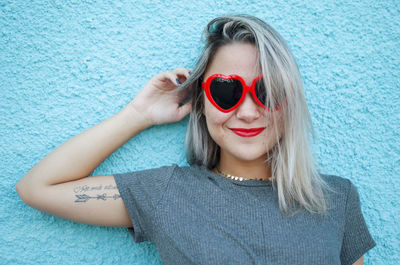 Portrait of woman wearing sunglasses and red lipstick against wall