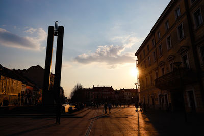 People walking on street amidst buildings against sky at sunset