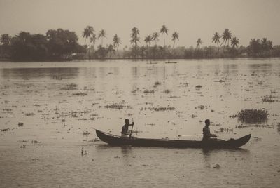 Silhouette people in boat sailing on river against sky