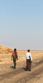 Rear view of men walking on desert against clear sky