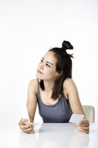 Young woman sitting on table against white background