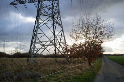 Electricity pylon on field by road against sky