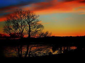 Silhouette trees by lake against sky during sunset