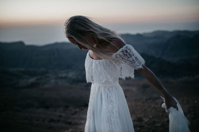 Midsection of woman standing on beach against sky during sunset