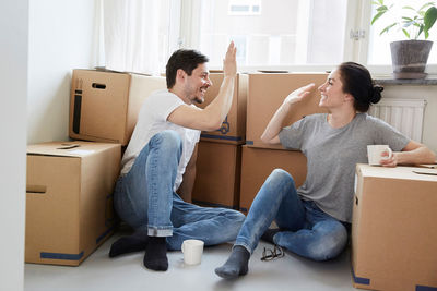 Happy couple giving high-five during coffee break while relocating in new house