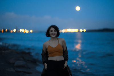 Portrait of smiling woman standing at beach against sky