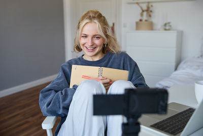 Portrait of young woman using digital tablet while sitting on bed at home