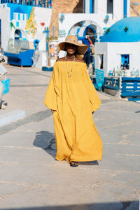 Beautiful african american woman in yellow dress and sun hat walks through streets with summer