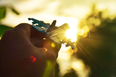 Cropped hand holding toy airplane during sunset