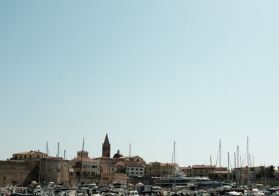 Sailboats moored on harbor by buildings against clear sky