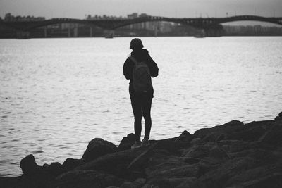 Rear view of silhouette man standing on rock by sea