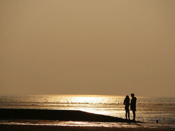 Silhouette people on beach against clear sky during sunset