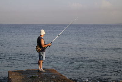 Man fishing on concrete jetty in sea against sky