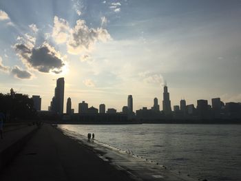 City buildings by sea against sky during sunset