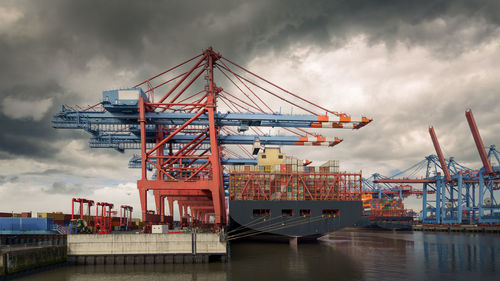 Cranes at commercial dock against sky