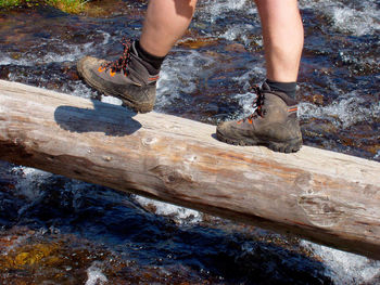 Low section view of man crossing flowing stream of water in forest