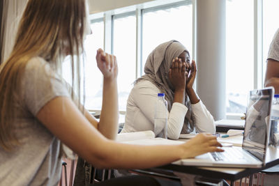 Smiling woman sitting with friend at desk in classroom university