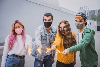 Smiling friends wearing mask holding sparklers outdoors