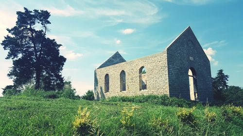 Old ruin by grassy field against sky