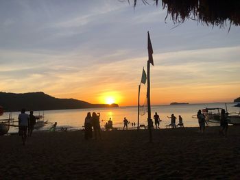 Silhouette people on beach against sky during sunset