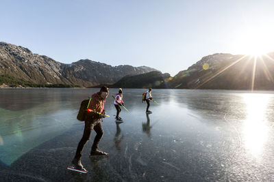 Friends ice-skating on frozen lake at sunset