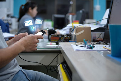 Midsection of man using phone with digital icon while working at desk